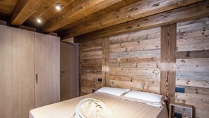 Ein Schlafzimmer mit einer Wand aus Holzlamellen, einem Bett mit weißen Leinen, einem roten Sessel und einem Holzschrank.