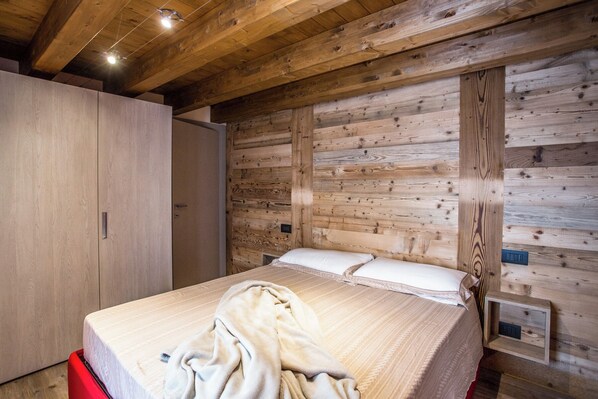 Un dormitorio con pared de listones de madera, cama con ropa de cama blanca, una silla roja y un armario de madera.