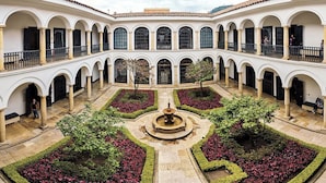 A courtyard with a central fountain, surrounded by symmetrical flower beds and white walls with arched windows. - Las Aguas Inner Experience (Bogotá)