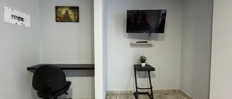 A small office space with a desk, chair, TV, and a small plant.