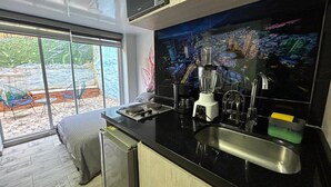 A modern kitchen with a black countertop, stainless steel sink, and a blender. There is a window with a view of a garden and a cityscape. - Las Aguas Inner Experience (Bogotá)