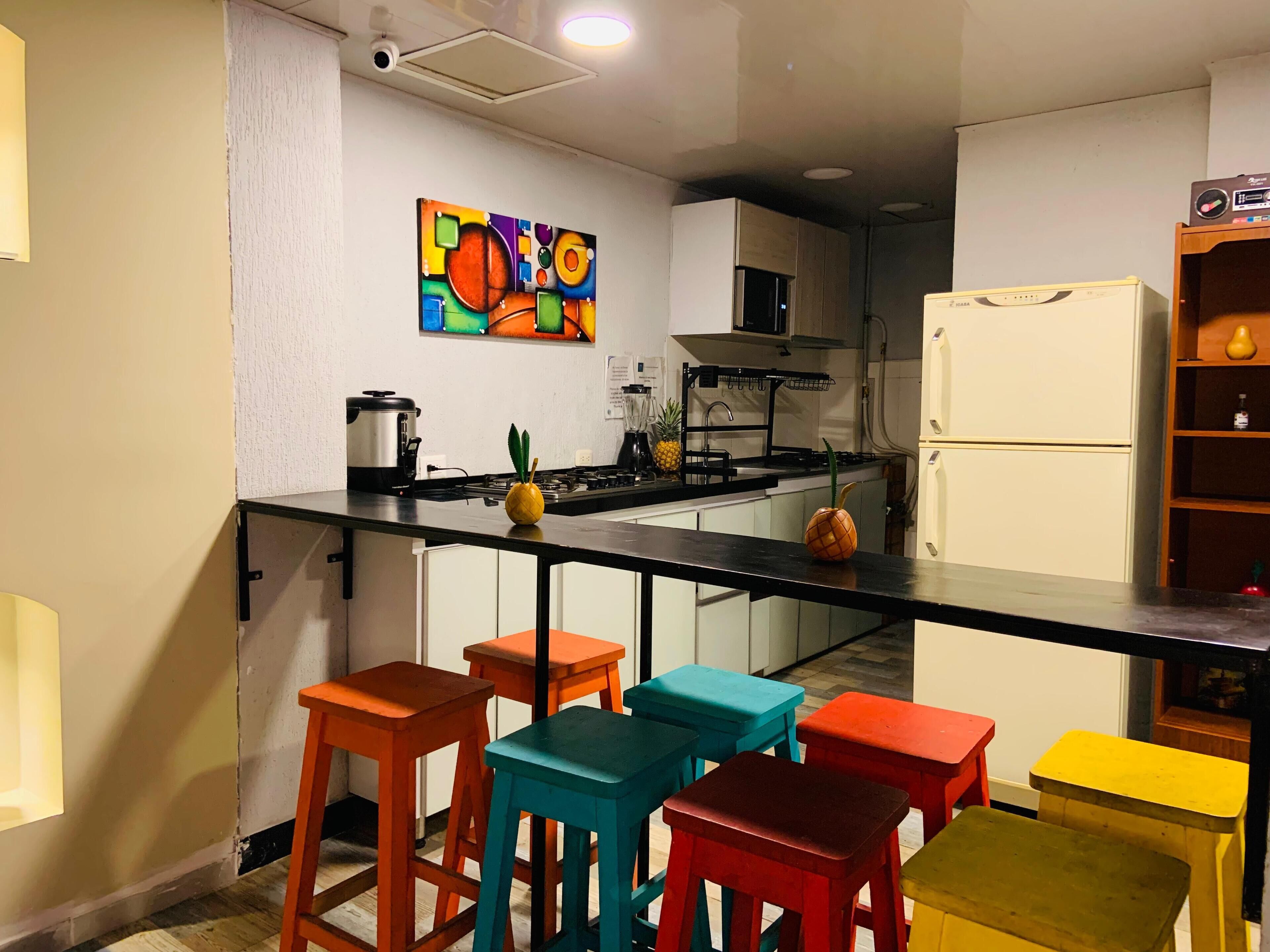 A compact kitchen with a black countertop, a stove, a refrigerator, and a colorful abstract painting on the wall.