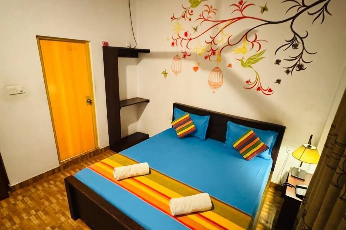 A room with a bed, a ceiling fan, a wall mural, and a door.