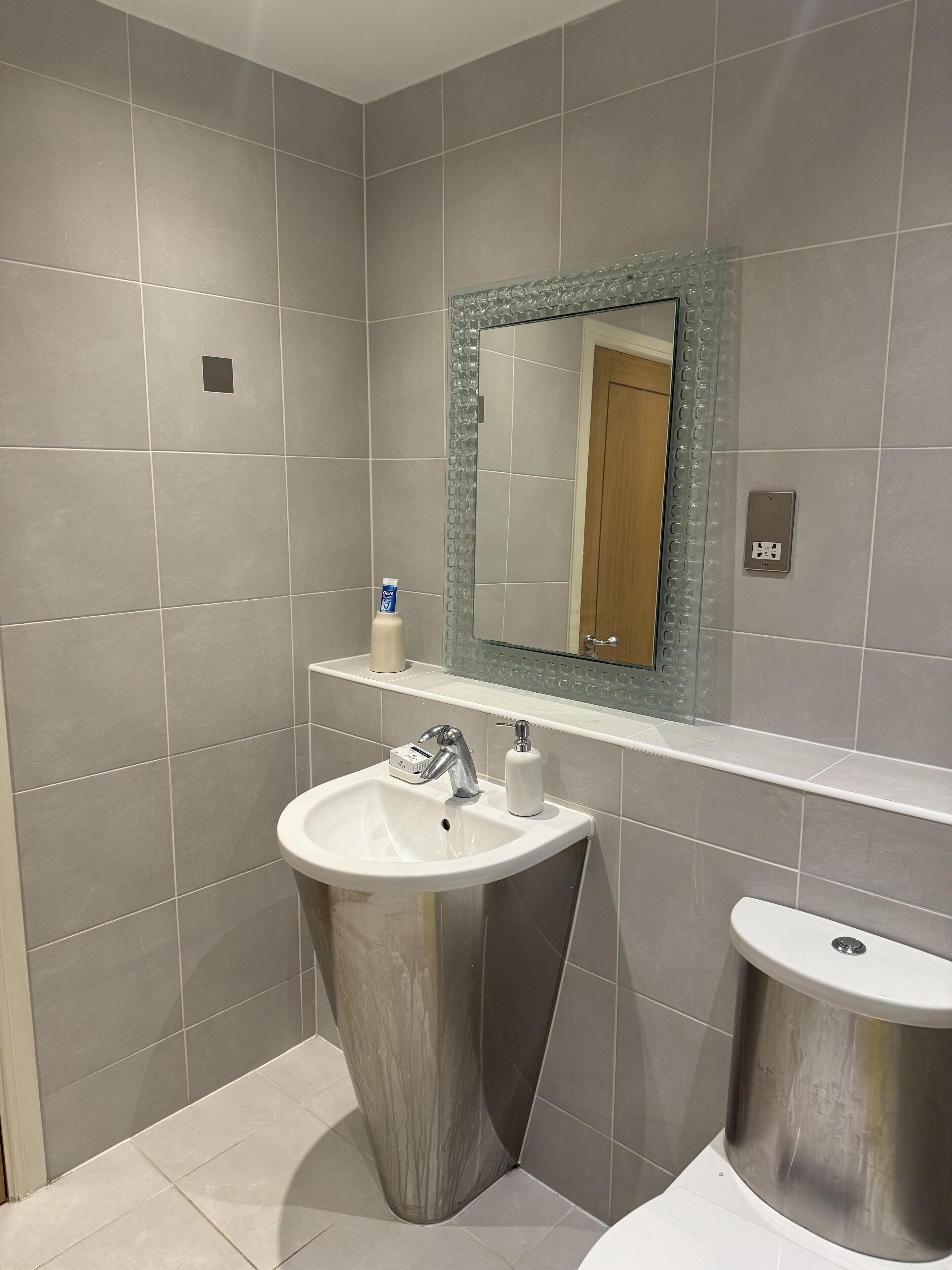 Une salle de bain moderne avec des carreaux gris, un lavabo blanc, un miroir doté d’un cadre décoratif et des toilettes.