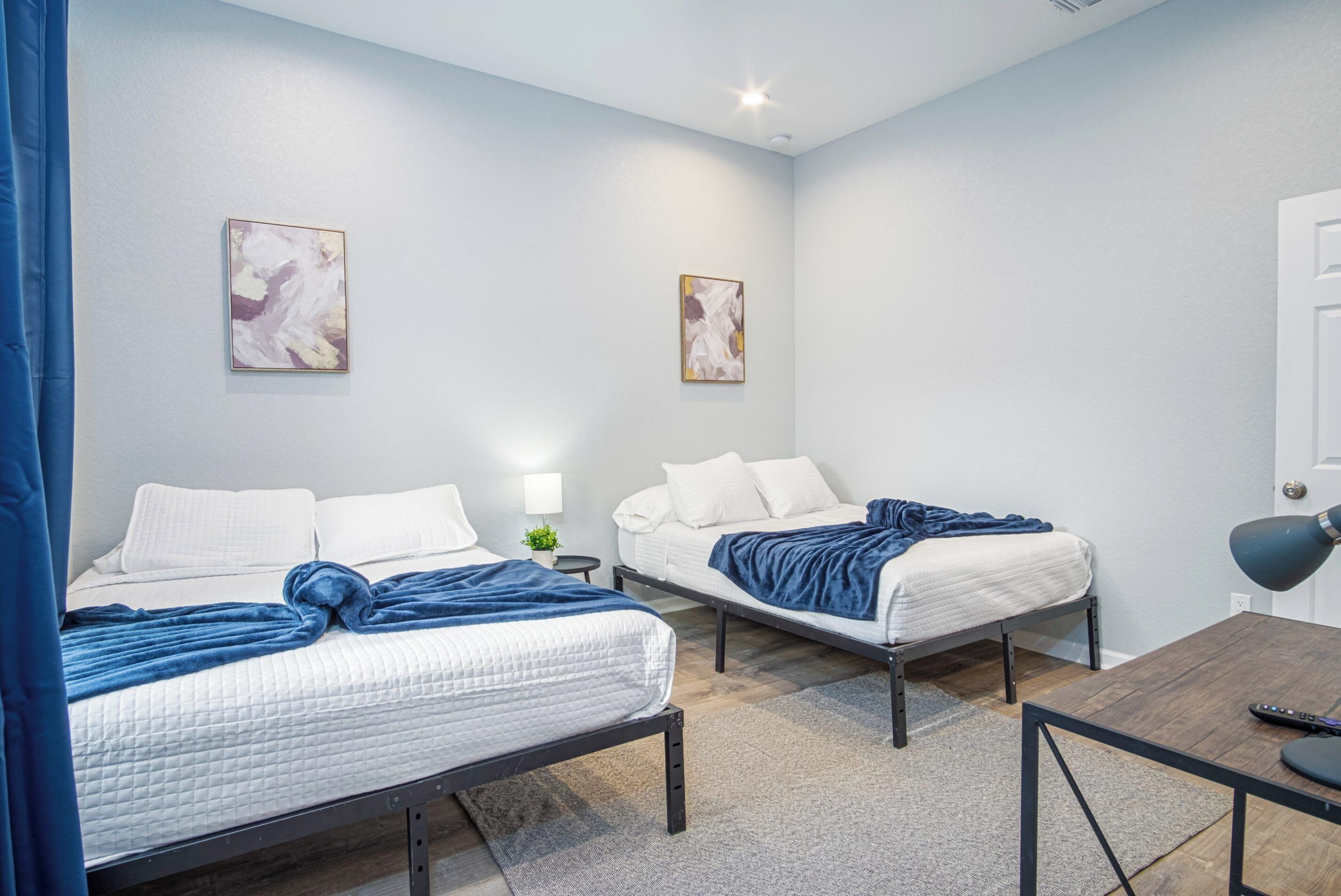 A hotel room with two beds, a desk, and a lamp.
