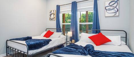 Two single beds with headboards, a window with curtains, and a wall with abstract art.