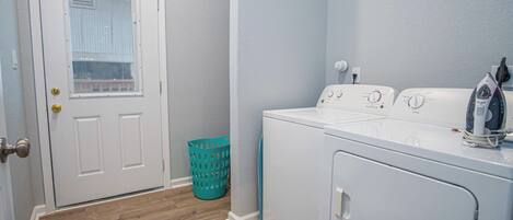 A laundry room with a front-loading washer and dryer, a door with a window, and a teal laundry basket.