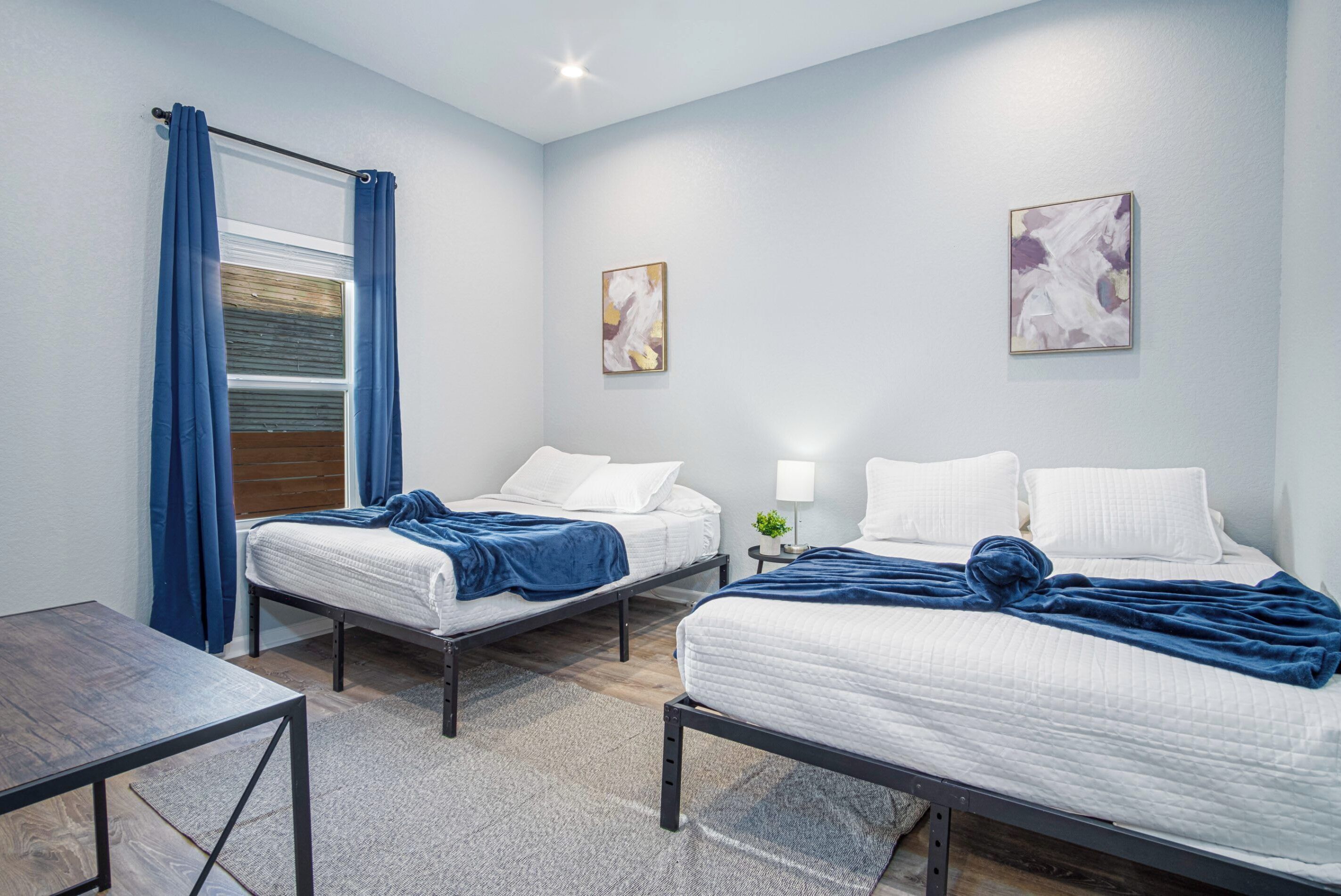 Une chambre d’hôtel avec deux lits, une petite table et une fenêtre avec des rideaux.