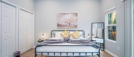 A bedroom with a bed, a nightstand, a lamp, a window, and a painting on the wall.