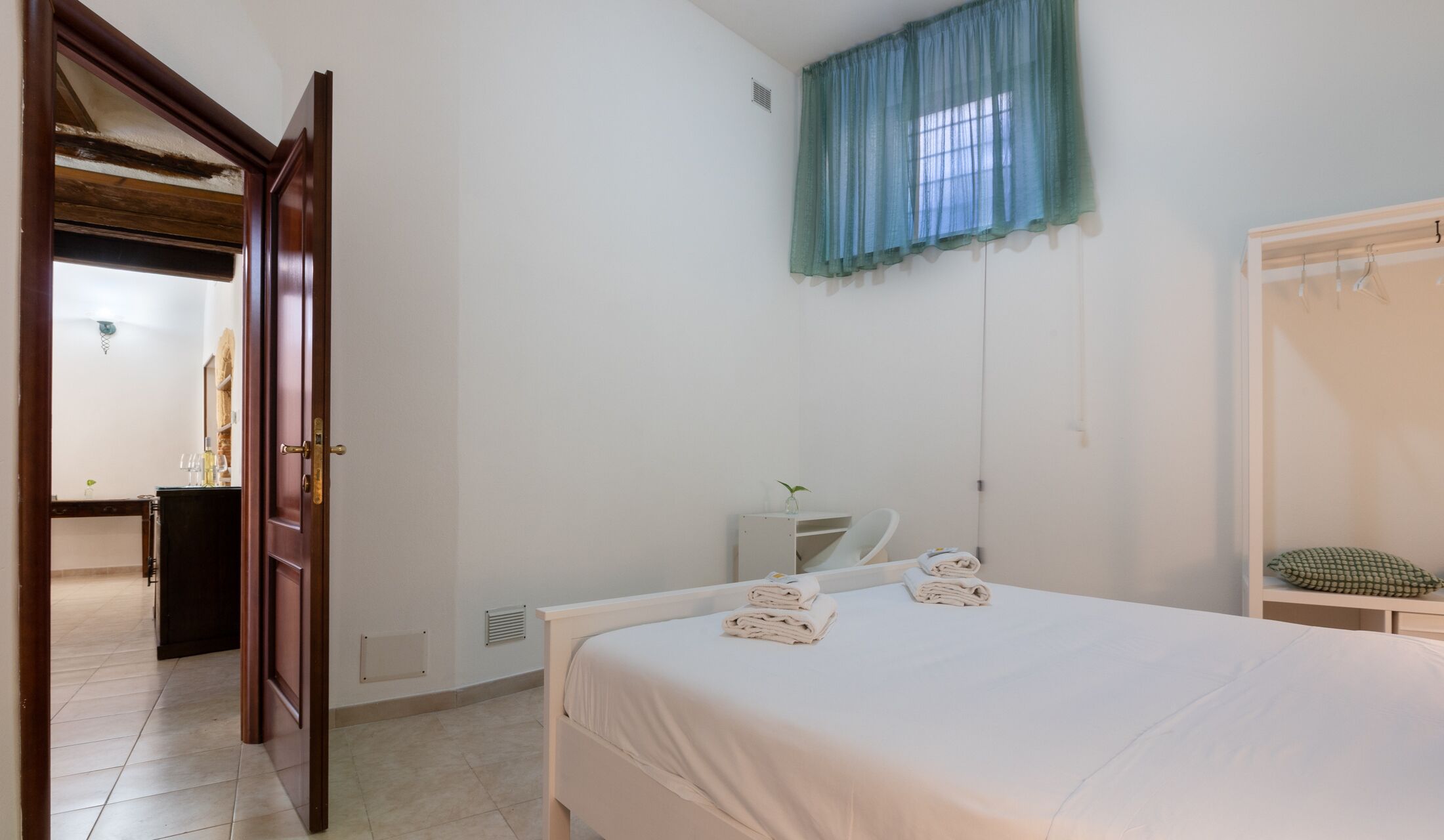 Une chambre à coucher comprenant un lit, une table de chevet, un miroir, une armoire et une salle de bain visible à travers une porte ouverte.
