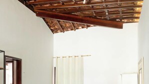Quarto com cama, televisão em uma cômoda e estrutura de teto em madeira.