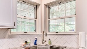 A kitchen with two windows, a sink, and a countertop with cleaning supplies. - Historic Route 66 Hideaway (Bristow)