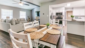 A modern kitchen with white cabinets, a microwave, and a stove. There is a dining table with woven placemats and white chairs. - Historic Route 66 Hideaway (Bristow)