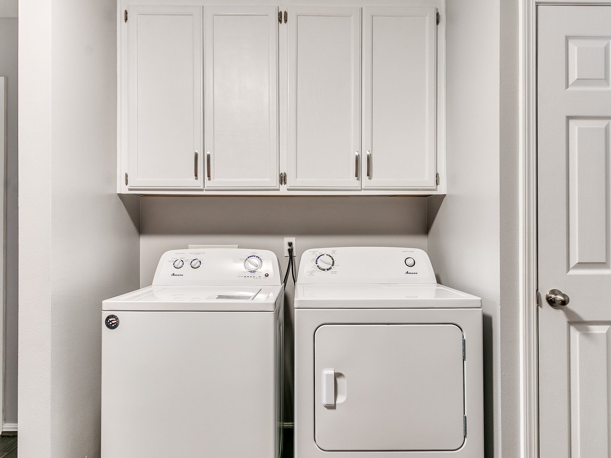 Une buanderie équipée de deux appareils électroménagers blancs, un lave-linge à chargement frontal et un sèche-linge à chargement par le haut, et de placards blancs au-dessus.