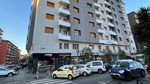 A multi-story building with balconies, a pedestrian crossing, and parked cars.