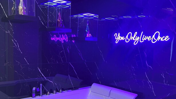 A modern bathroom with a large bathtub, marble walls, and neon signage.