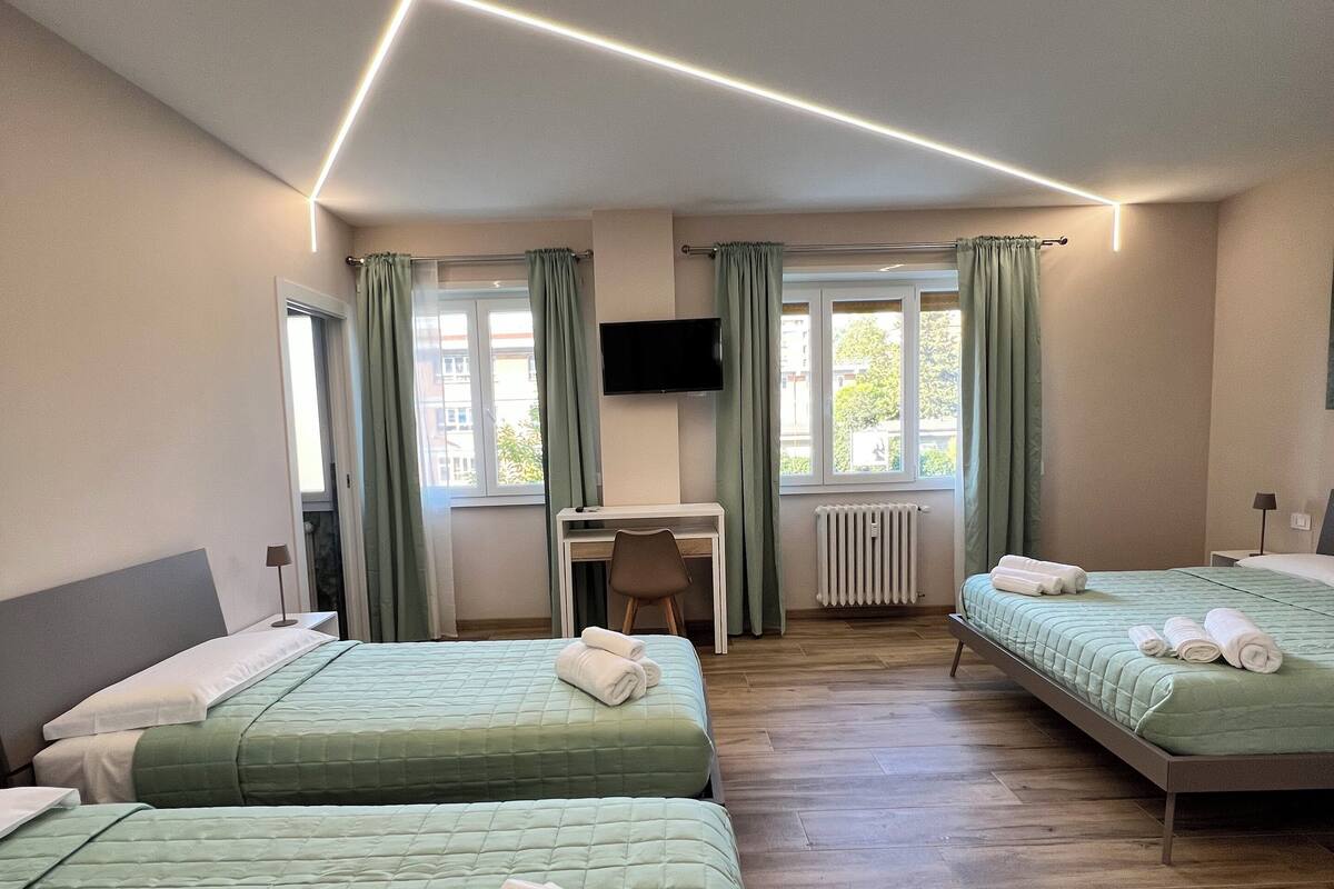 A hotel room with two beds, a desk, a TV, and a view of the outside.