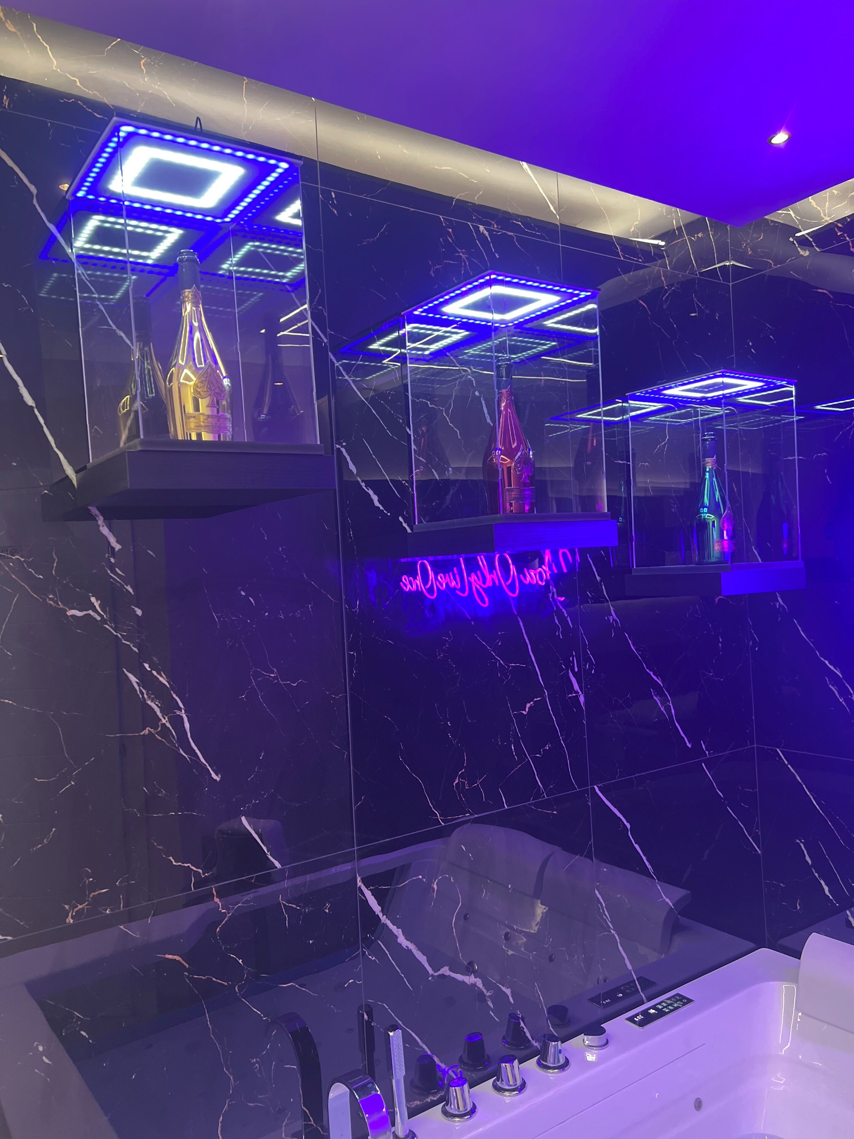 A modern bathroom with marble walls, a bathtub, and illuminated geometric light fixtures.