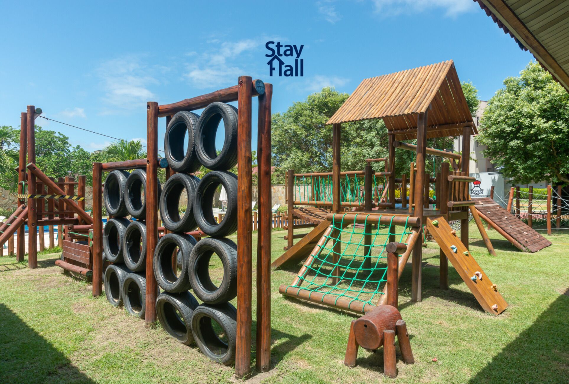 A playground with tire climbing structures, a rope net, and a wooden playhouse.