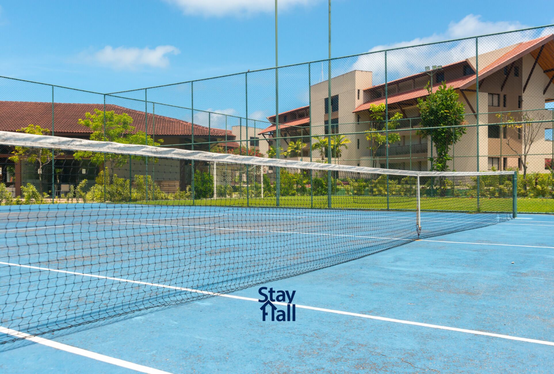 A tennis court with a net in the middle, surrounded by a fence.