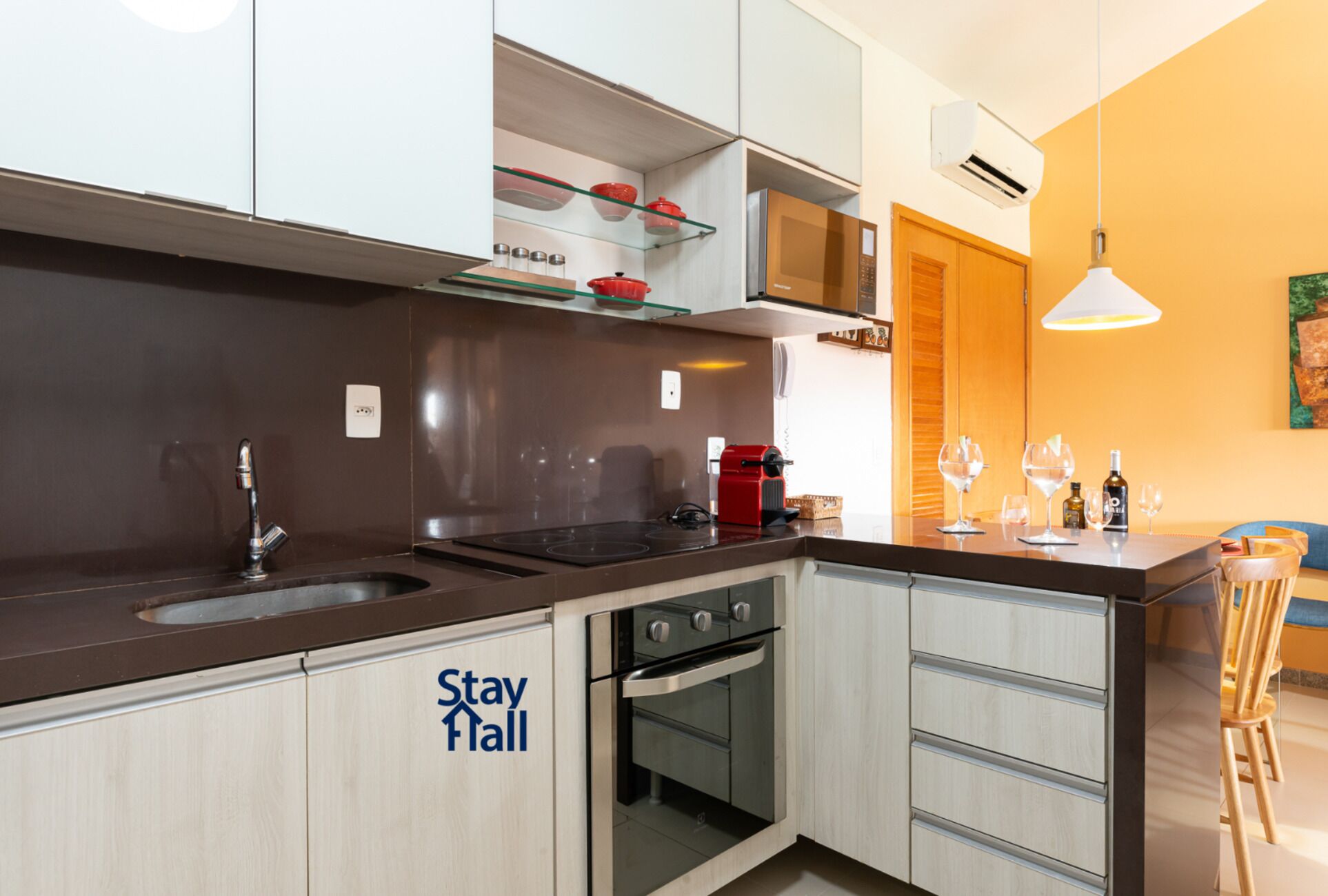 A modern kitchen with a built-in oven, a microwave, and a sink. There is a 'Stay Hall' sign on the cabinet.