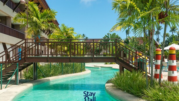 Zona de piscina con un puente, palmeras y un letrero que dice 'Stay at'.