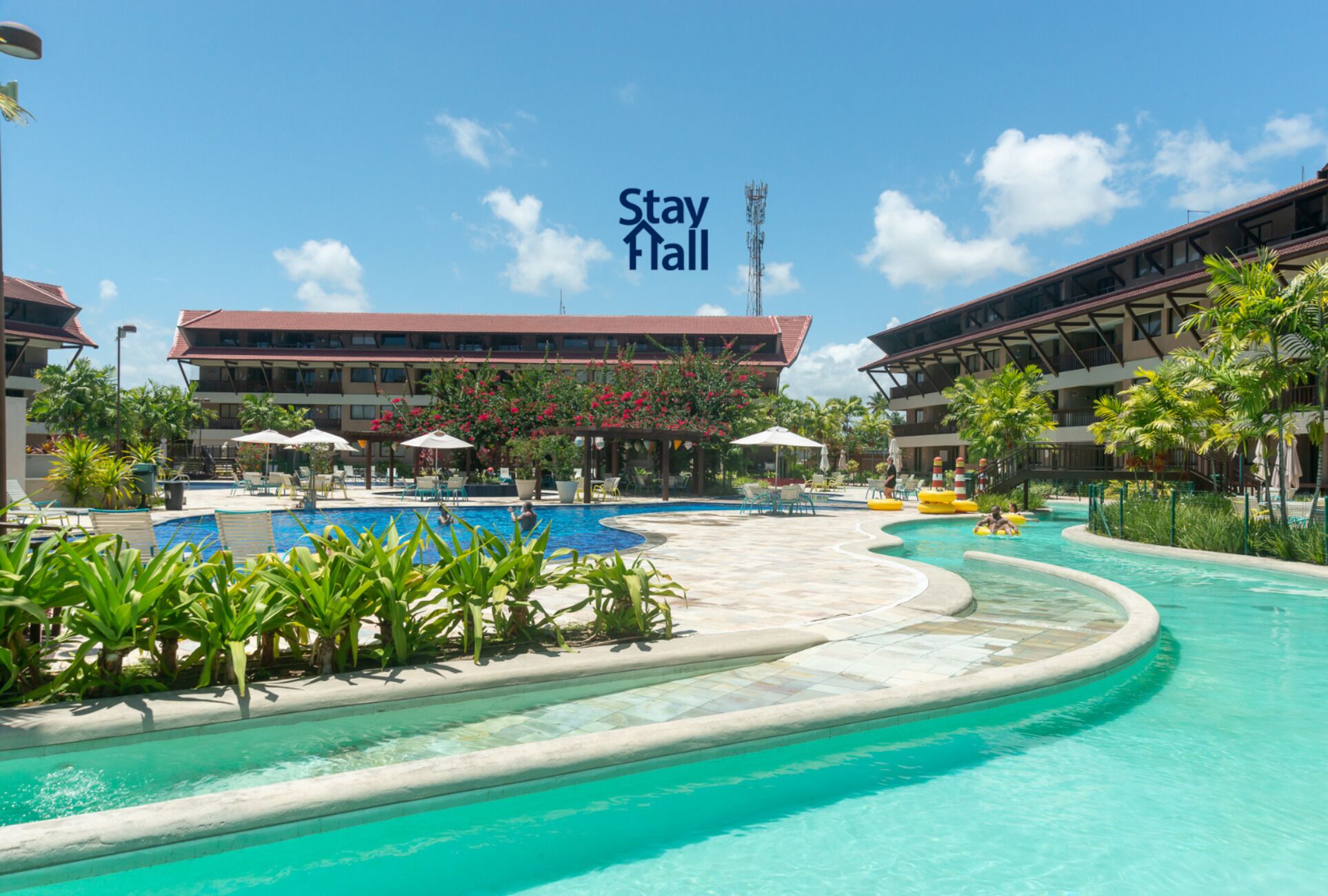 A resort pool area with a large pool, lounge chairs, and a building with balconies.