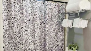 Un baño con cortina de ducha estampada con motivos de paisley, un inodoro, un lavabo con espejo y un perchero con toallas.