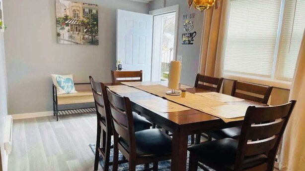 Un comedor con mesa de madera, seis sillas, una araña y un cuadro de arte con vista a la ciudad.