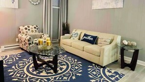 Una sala de estar con un sofá color crema, un tapete estampado, una mesa de centro de vidrio, un sillón con estampado de lunares y una pequeña mesita auxiliar.