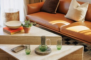 A living room with a leather sofa, a coffee table with decorative items, and a bookshelf with books. - Sophisticated Studio Flat With Rooftop Access (London)