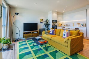 A modern living room with a sofa, a coffee table, and a TV. There is a kitchen area in the background. - Modern Studio Flat in North London (London)