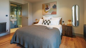 A modern bedroom with a large bed, a bedside table with a lamp, a mirror, and a bathroom visible through a glass door. - Modern Studio Flat in North London (London)