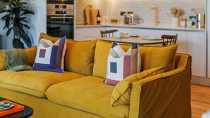 A modern living room with a mustard-colored sofa, a coffee table, and a dining area in the background. - Modern Studio Flat in North London (London)