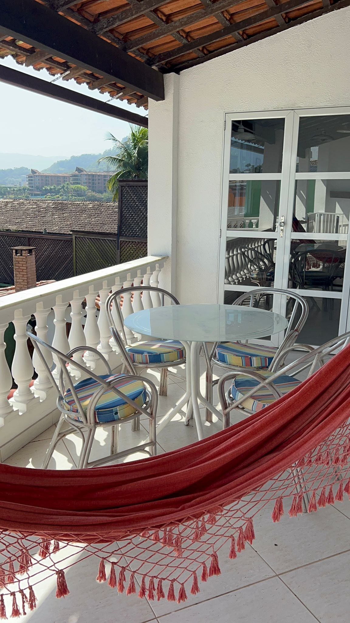 Ein Balkon mit weißer Reling, einem Glastisch mit Stühlen und einer roten Hängematte.
