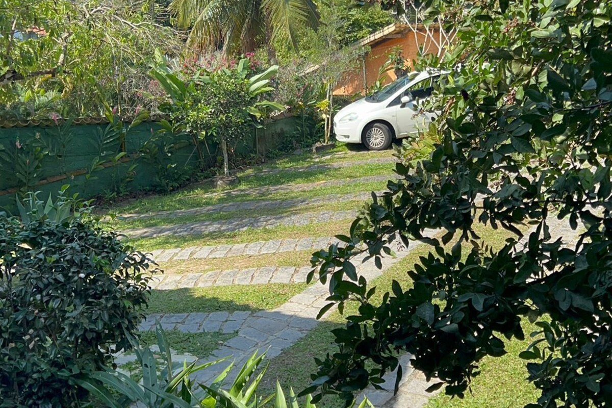 A white car parked on a paved driveway with a lush garden and a mountain in the background.