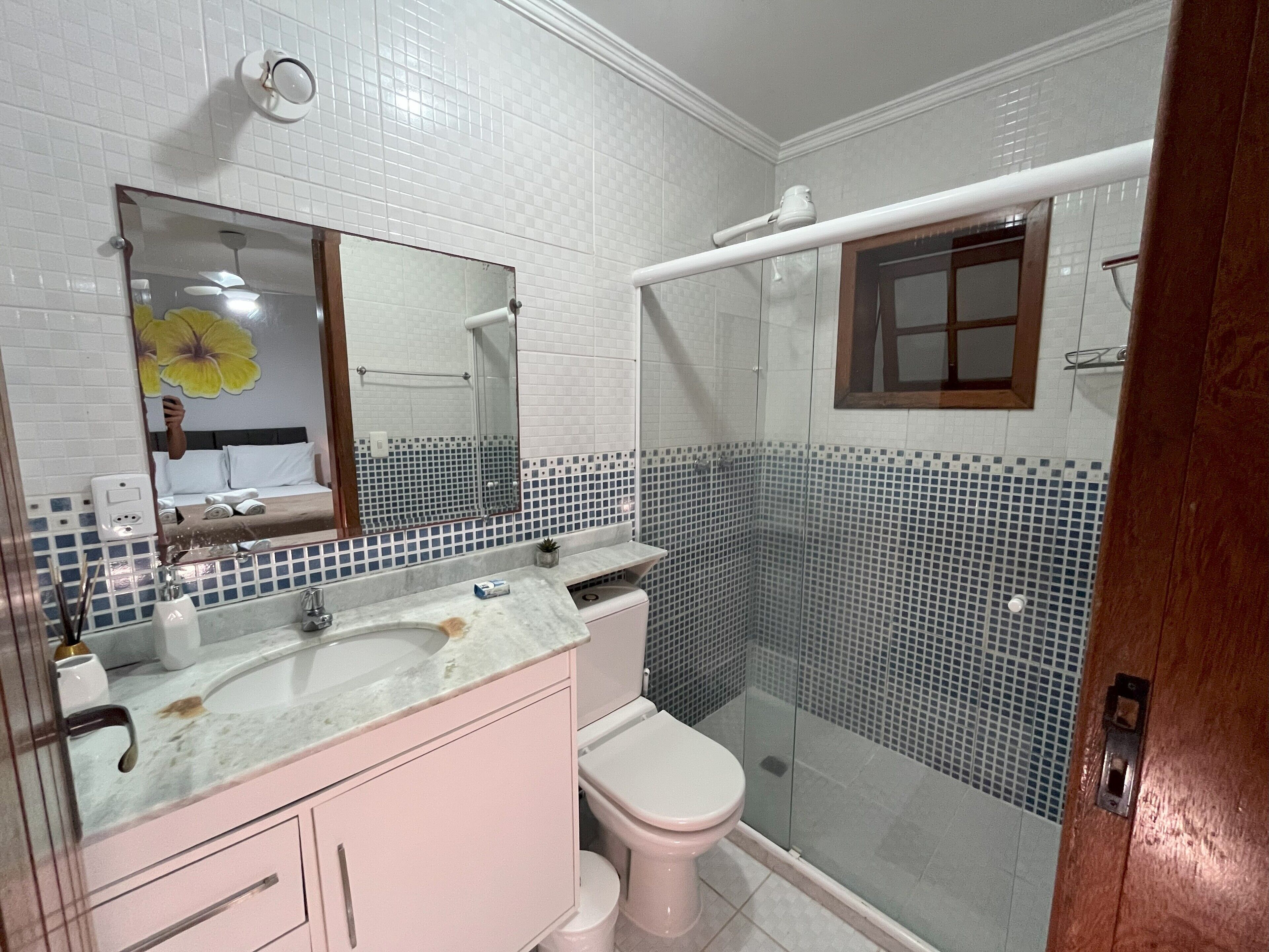 Un baño con lavamanos de mármol, inodoro y cabina de ducha con mampara de vidrio.