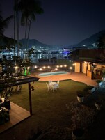 A nighttime view of a pool area with a dining setup and a view of a cityscape in the background.