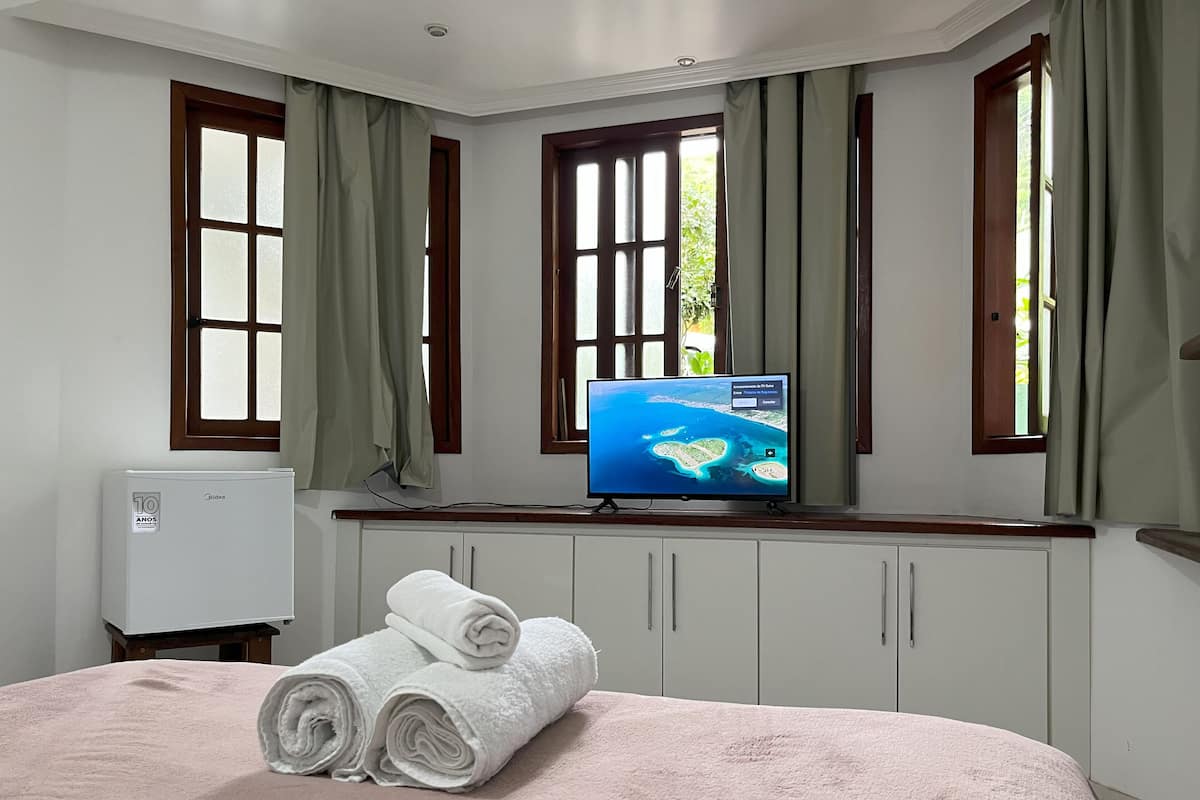 Une chambre d’hôtel avec un lit, un téléviseur fixé au mur et une fenêtre avec des rideaux.