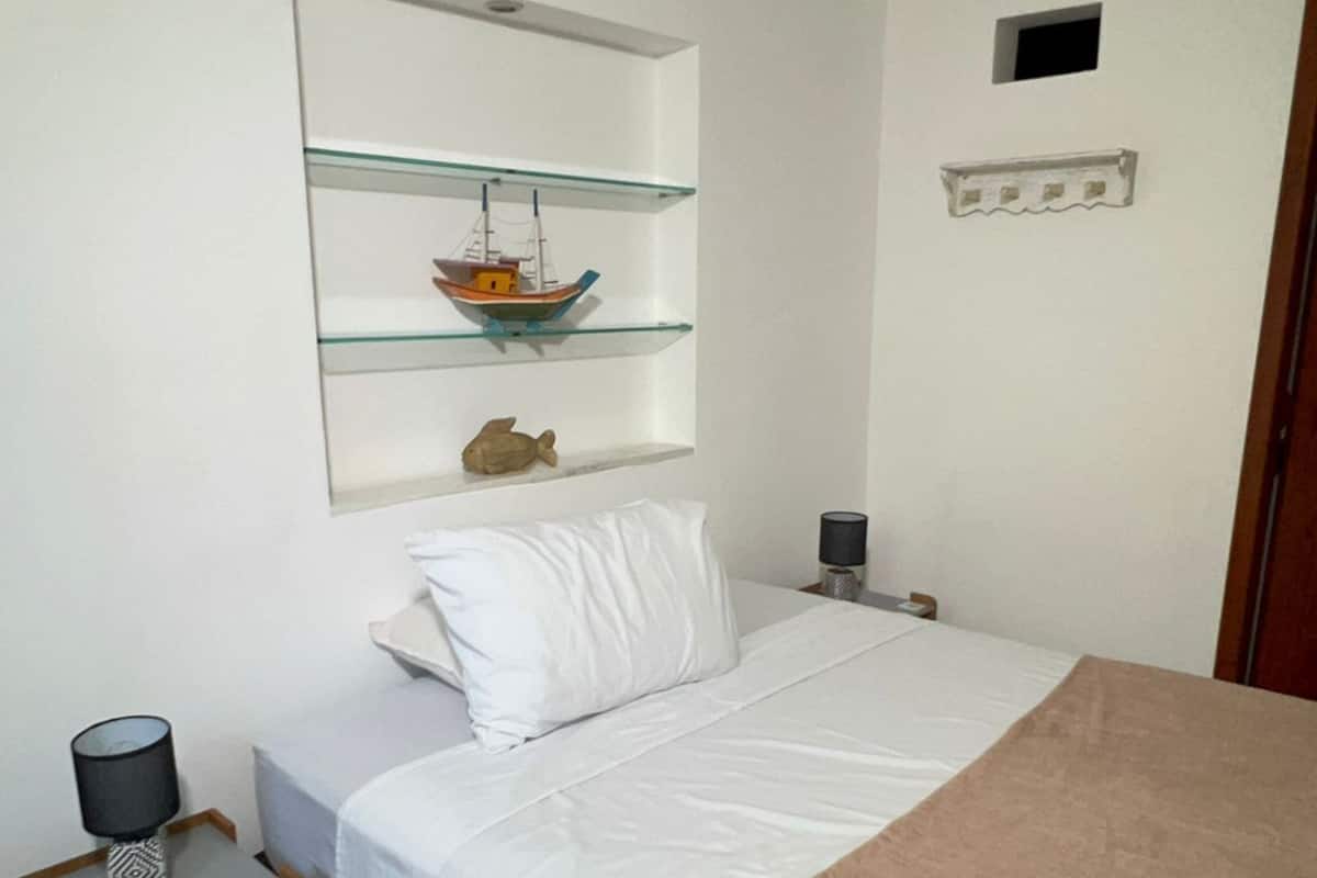Une chambre à coucher comprenant un lit, une table de chevet avec une lampe, une étagère avec des objets décoratifs et une porte.