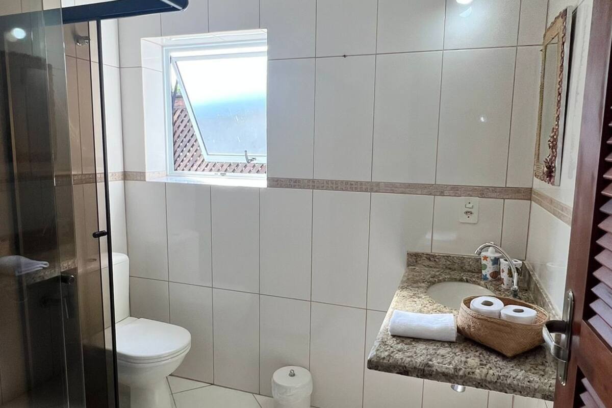 Une salle de bain avec une douche à parois de verre, des toilettes, un lavabo avec un plan de travail et une petite fenêtre.