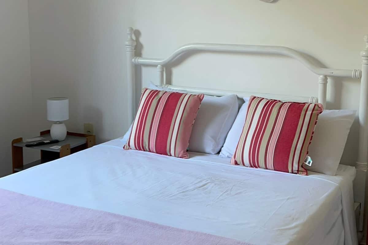 Un lit bien fait, avec une tête de lit blanche, deux oreillers à rayures et une grande décoration florale rose accrochée au mur.
