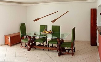 A dining area with a glass table, green upholstered chairs, and a fruit bowl.
