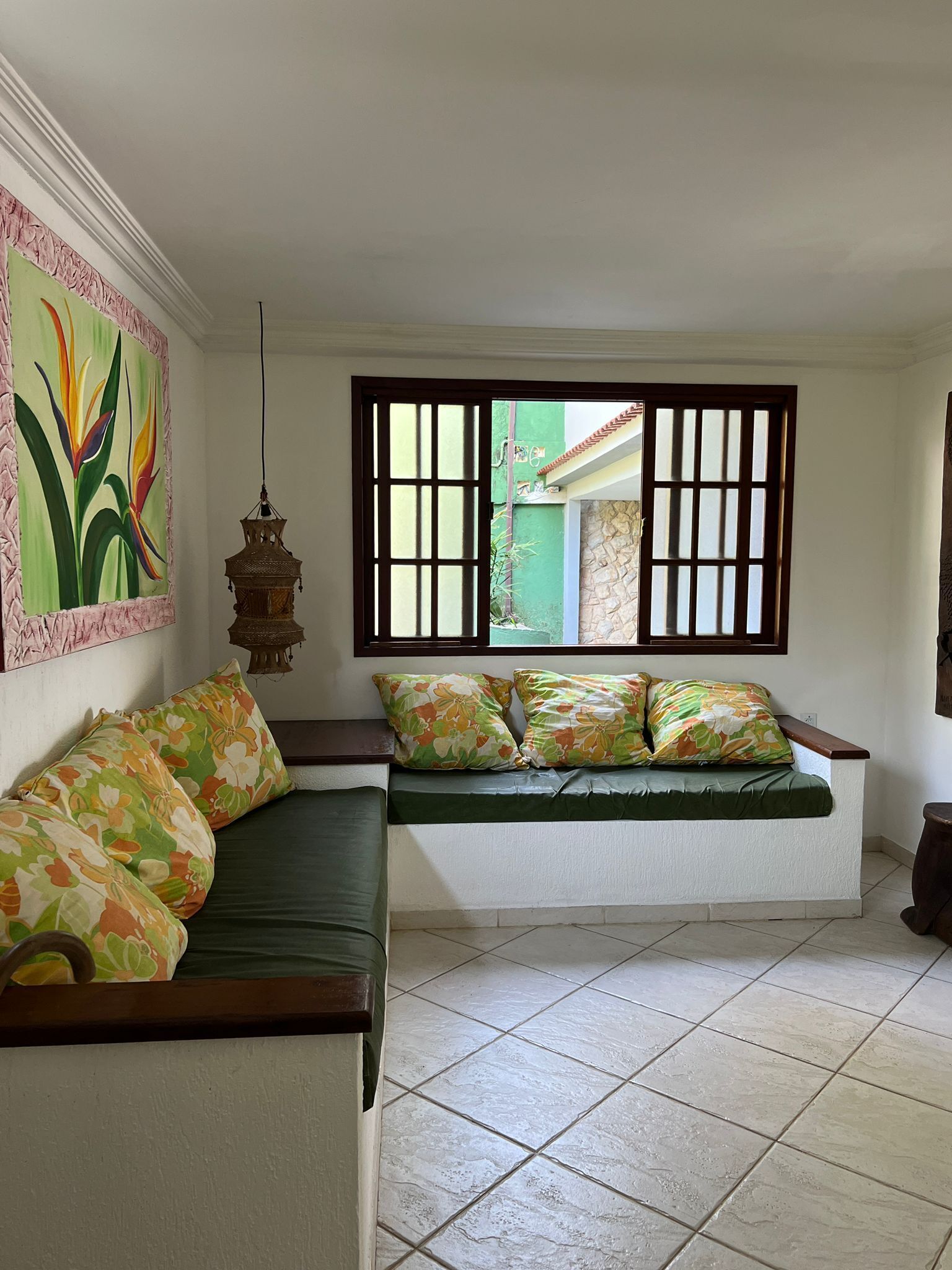 Una habitación con sofá, ventana con rejas, un farol colgante y un cuadro en la pared.