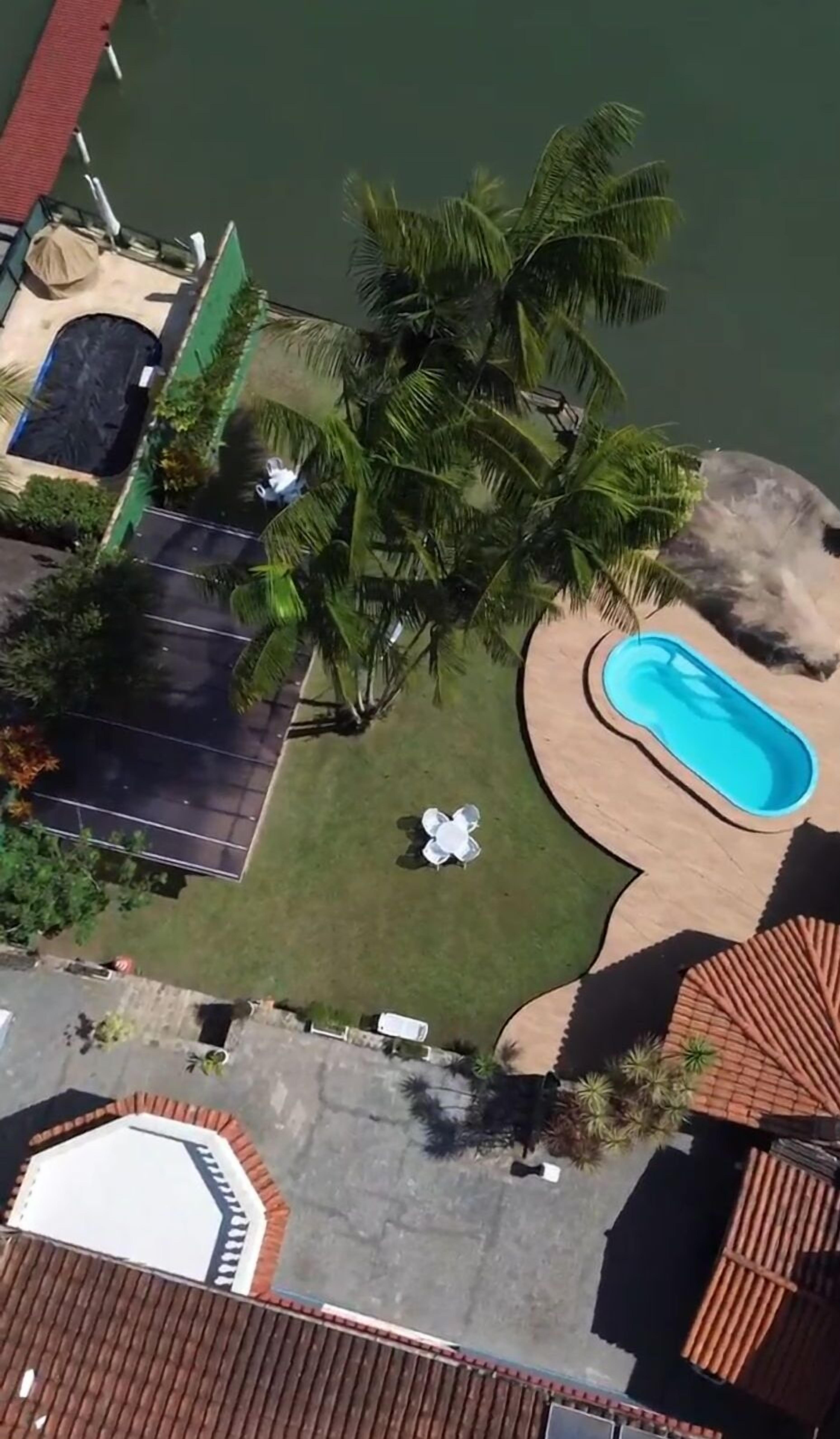 An aerial view of a residential area with a swimming pool, a covered patio, and a lawn with palm trees.