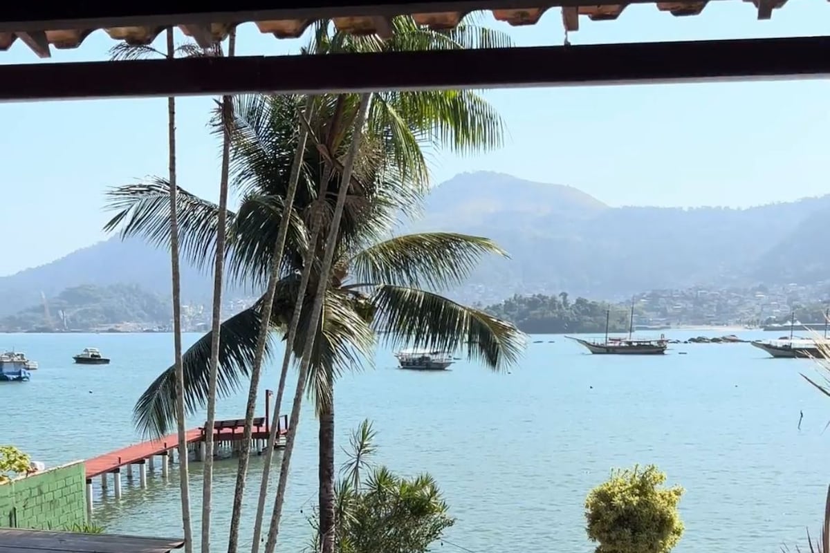 A balcony with a view of a calm sea, boats, and palm trees.