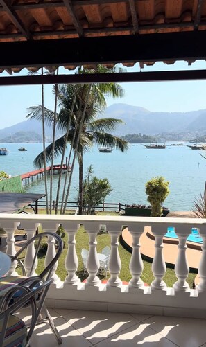 A balcony with a view of a calm sea, boats, and palm trees. - Casa das Tartarugas (Angra dos Reis)