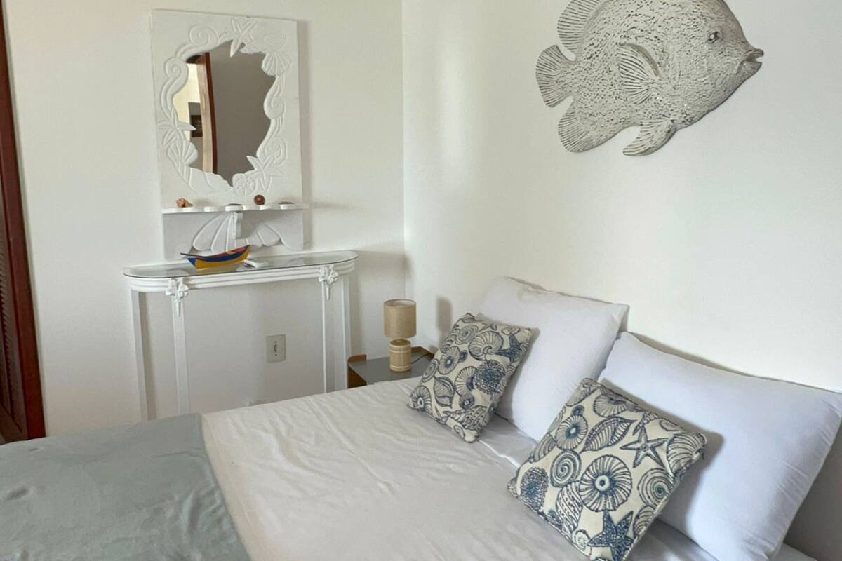 Une chambre à coucher comprenant un lit, des oreillers, une table de chevet, une commode, un miroir et un élément de décoration murale.