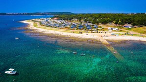 Vista aérea de un complejo turístico costero con aguas cristalinas, una playa de arena y una hilera de villas.