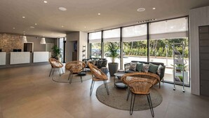 Un vestíbulo espacioso con muebles de mimbre, un mostrador de recepción y grandes ventanales que ofrecen vistas al exterior.